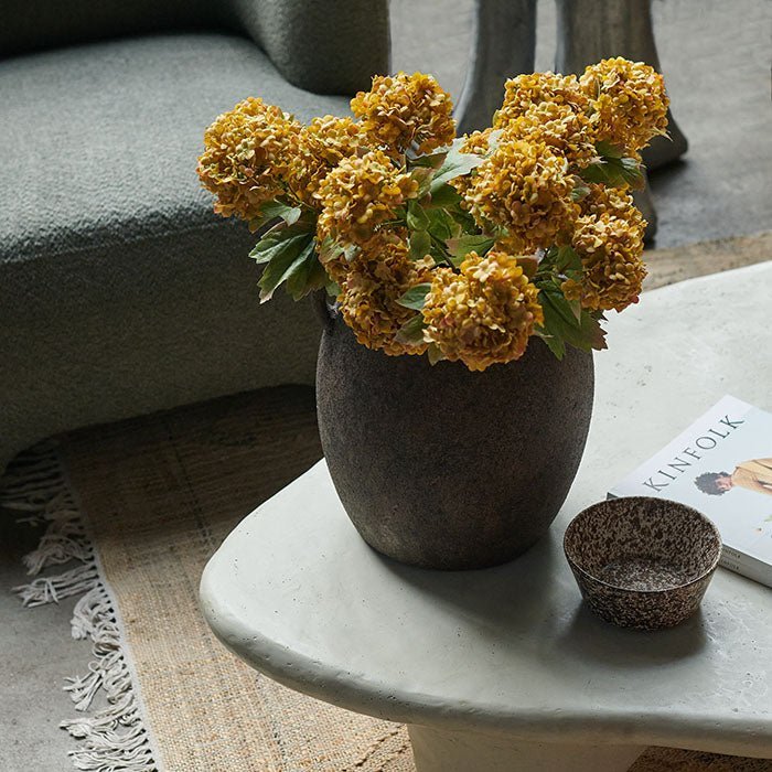 The Isador Vase, a rounded ceramic vase in a rustic brown finish with two handles, on a curved coffee table.