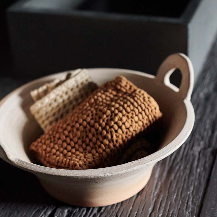 A close up of the Lucerne Terracotta Bowl. A traditional rustic terracotta bowl with handles styled with brown face towels.