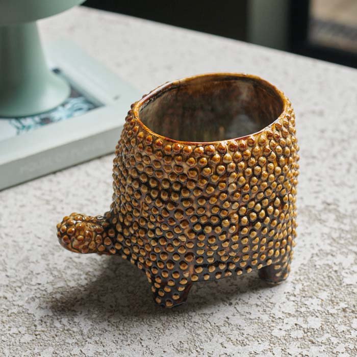 A brown ceramic pot with a raised texture in the shape of a tortoise.