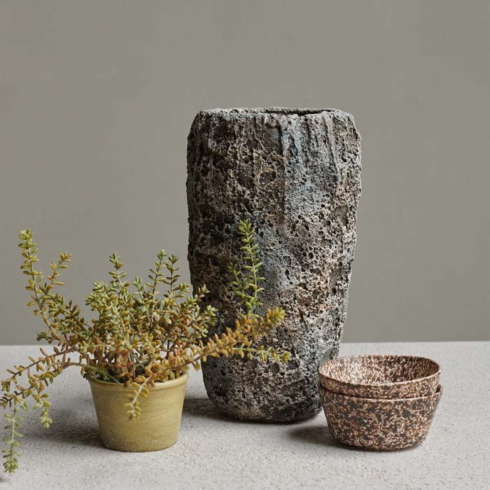 A large grey textural vase next to a small faux plant and some bowls