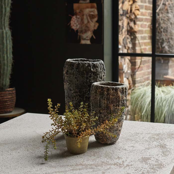 Two rough textured grey ceramic vases next to a small faux plant on a counter.