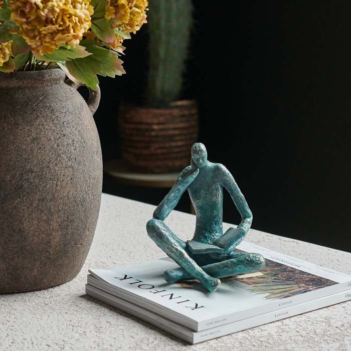 The Rollo Figurative Sculpture, a faux brass polyresin sculpture in a blue tone of a seated figure reading a book.