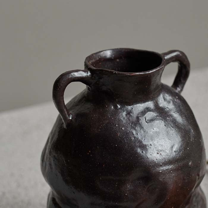 Detail of the organic finish on a dark brown ceramic vase with two small handles.