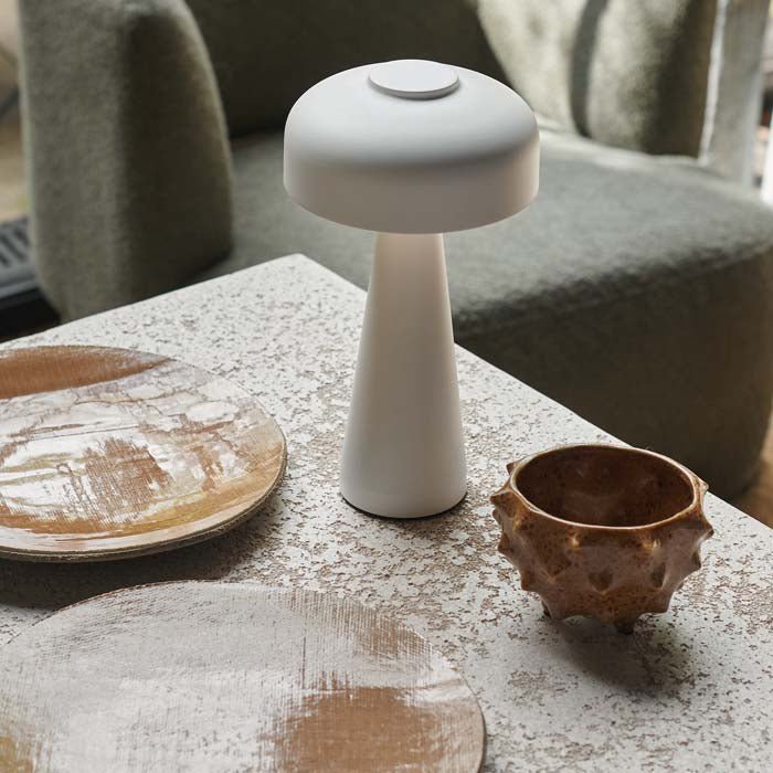 A modern rechargeable table lamp in a white finish next to some bowls.