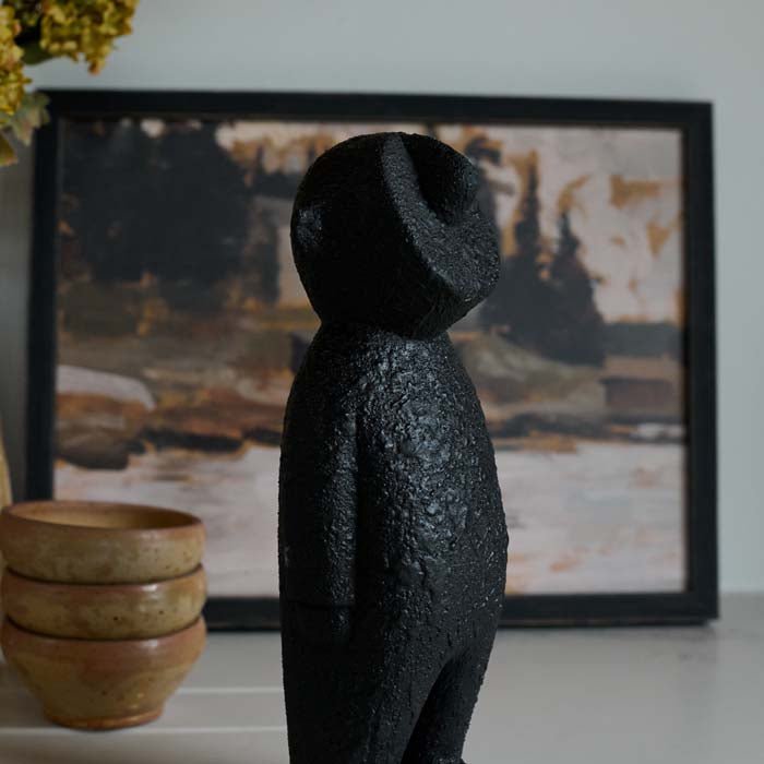 The Amethi Wooden Sculpture, a small figurative sculpture in black wood, next to a set of three glazed bowls.