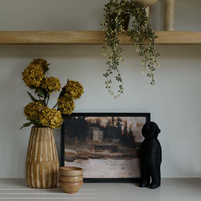 The Amethi Wooden Sculpture, a small figurative sculpture in black wood, next to a carved wooden vase and some faux florals.