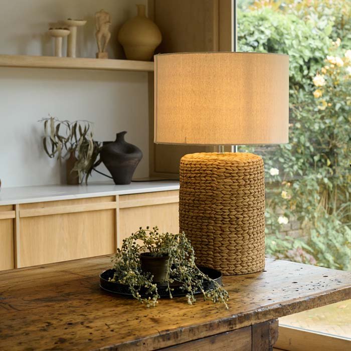 The Celano Rope Table Lamp, a cylindrical table lamp with a chunky knotted base and a natural coloured drum shade.