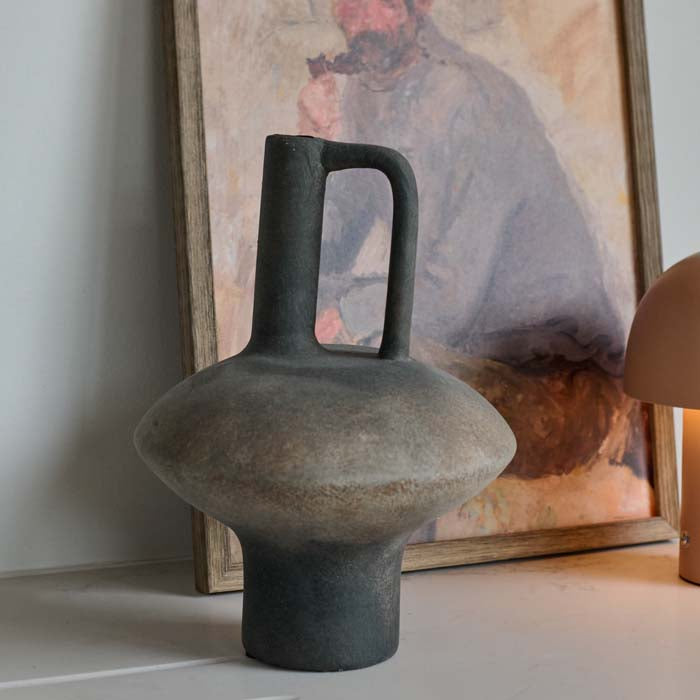 Lovina Vase. A modernist sculptural terracotta vase styled on a table with a male portrait in the background.