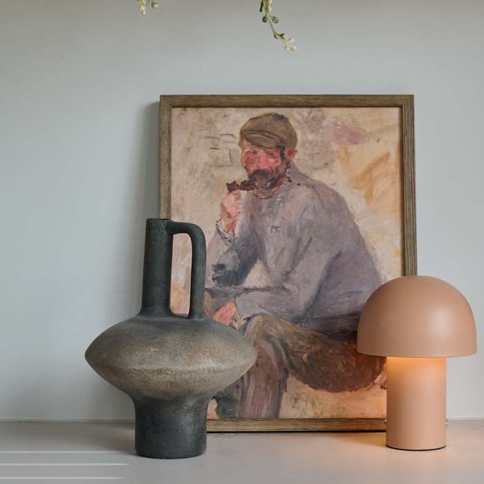 Lovina Vase. A modernist sculptural terracotta vase styled on a table with a male portrait in the background.