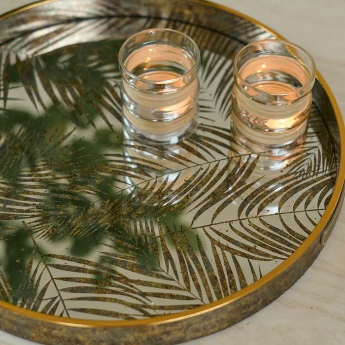 The Nassua Tray, a round tray with a mirrored surface featuring a botanical design, with a pair of glass votives.