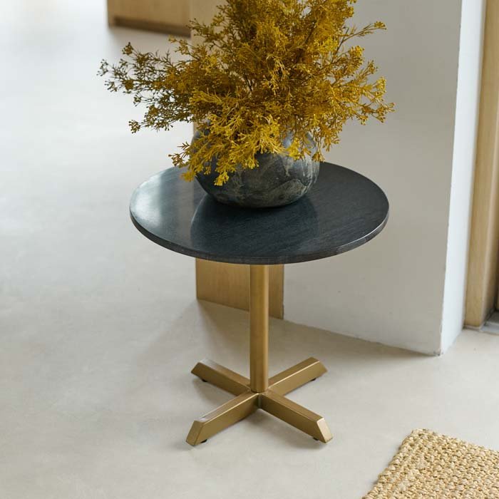 The Varana Round Side Table, with a dark organic shaped stone vase holding some vibrant mustard coloured faux floral stems.