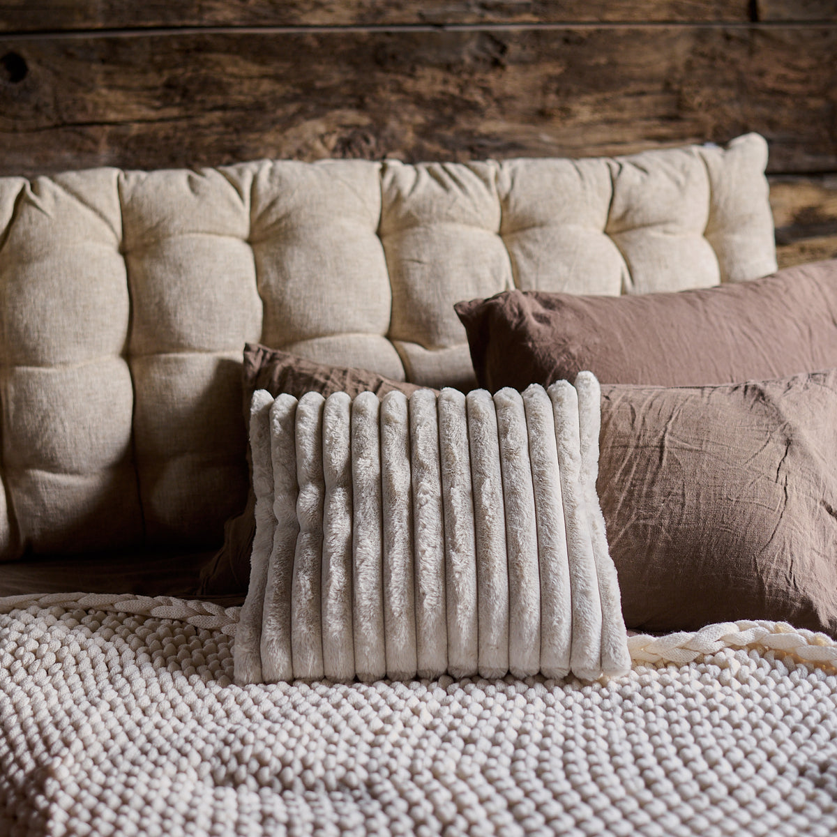 The Baxley Chunky Knit Throw on a bed with mismatched cushions in warm earthy tones.