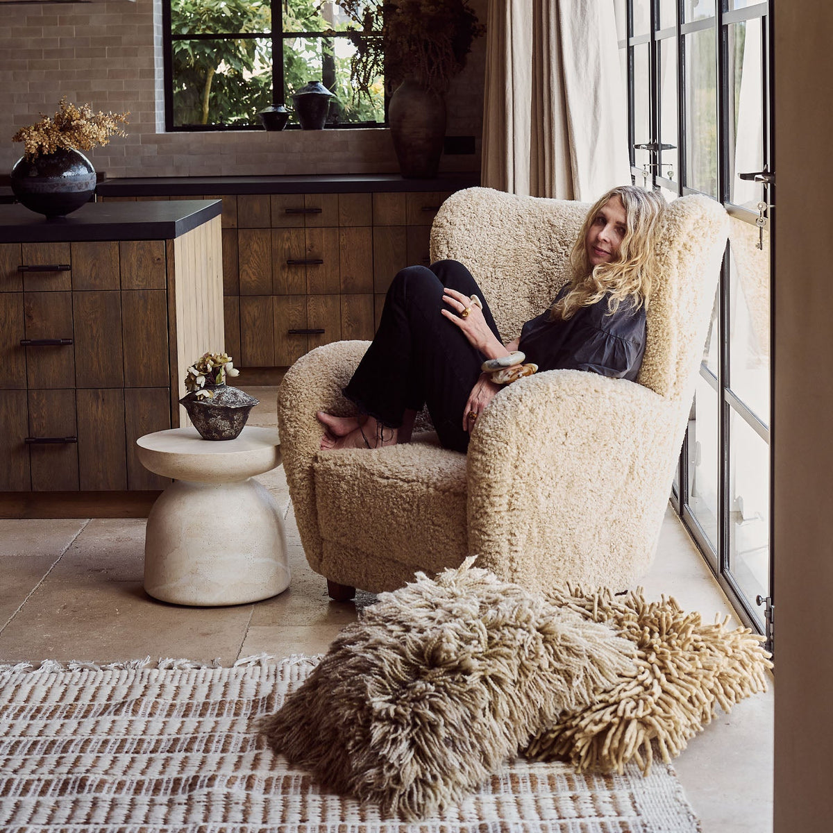 Abigail Ahern Karina Faux Fur Armchair in neutral cream faux fur with a soft, fluffy texture, rounded wingback silhouette and generously cushioned design for decadent comfort. styled in a living room 