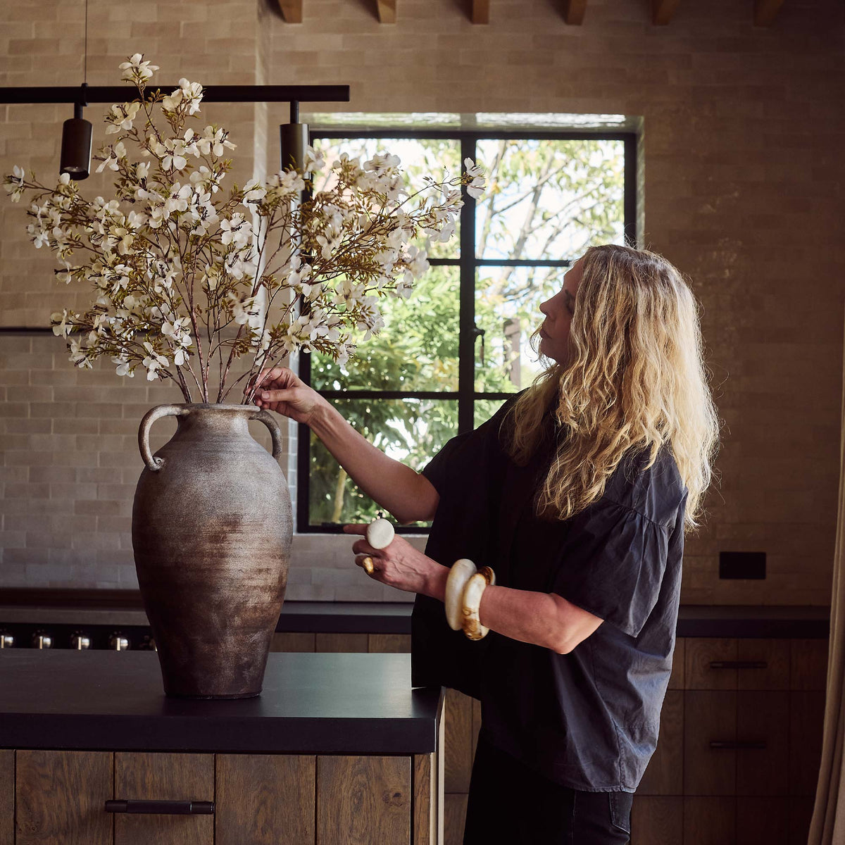 Interior designer Abigail Ahern arranging artificial flowers in a large vase in a kitchen.