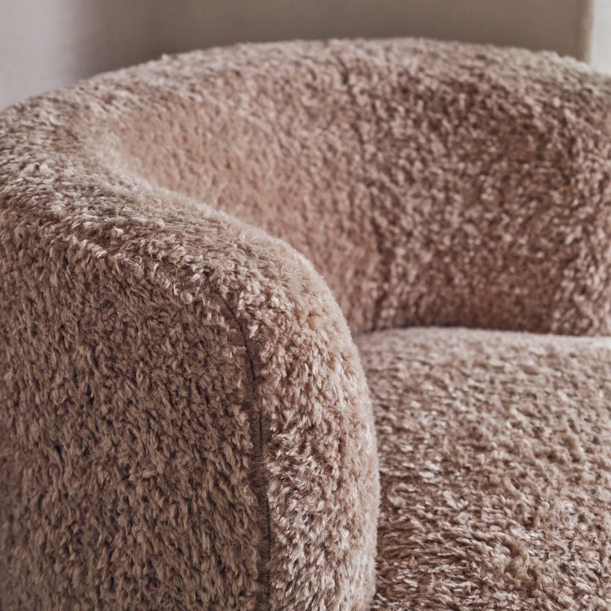 Close up of the Abigail Ahern Nola Armchair in a warm beige faux shearling finish, featuring a softly rounded modern silhouette with plush, tactile upholstery. Shown in a cosy contemporary interior with soft natural hues and layered textures, creating a warm and inviting space.