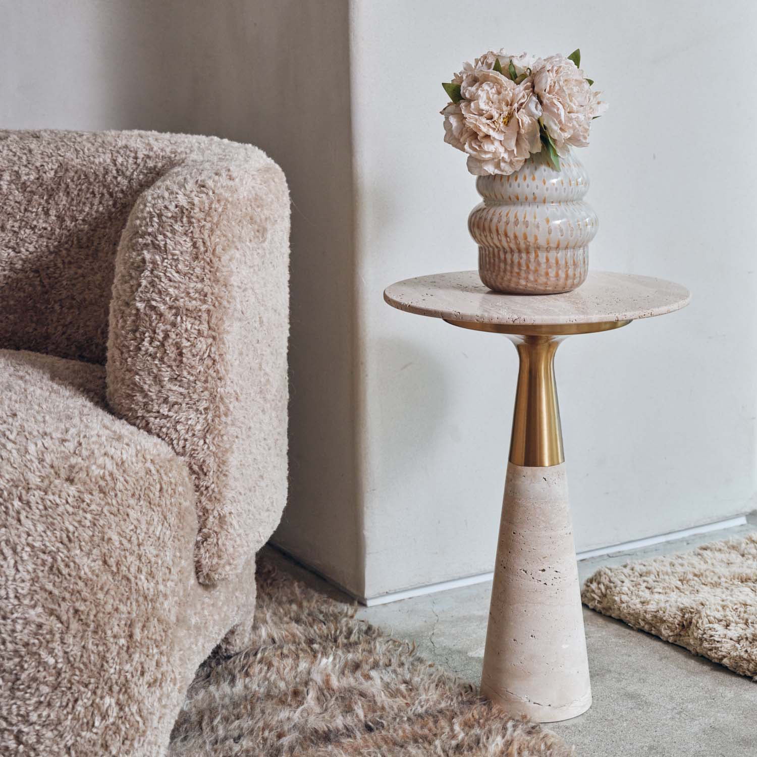 Abigail Ahern Daytona Marble Side Table with a sculptural marble top and brass detail, styled beside an upholstered armchair with a glass vase, creating an elegant and contemporary living space.