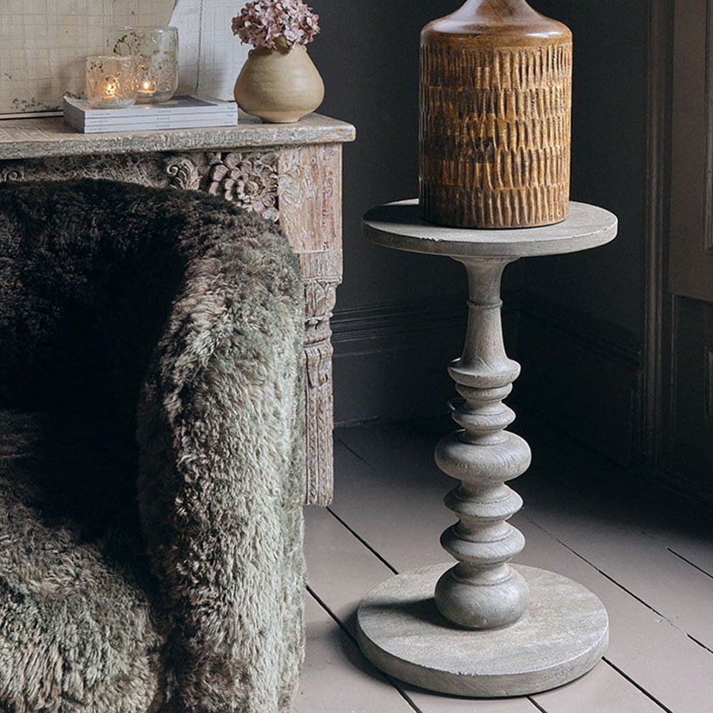 Abigail Ahern Devon Round Wooden Side Table with a natural suar wood finish and distinctive grain, styled beside an armchair as a versatile occasional table.