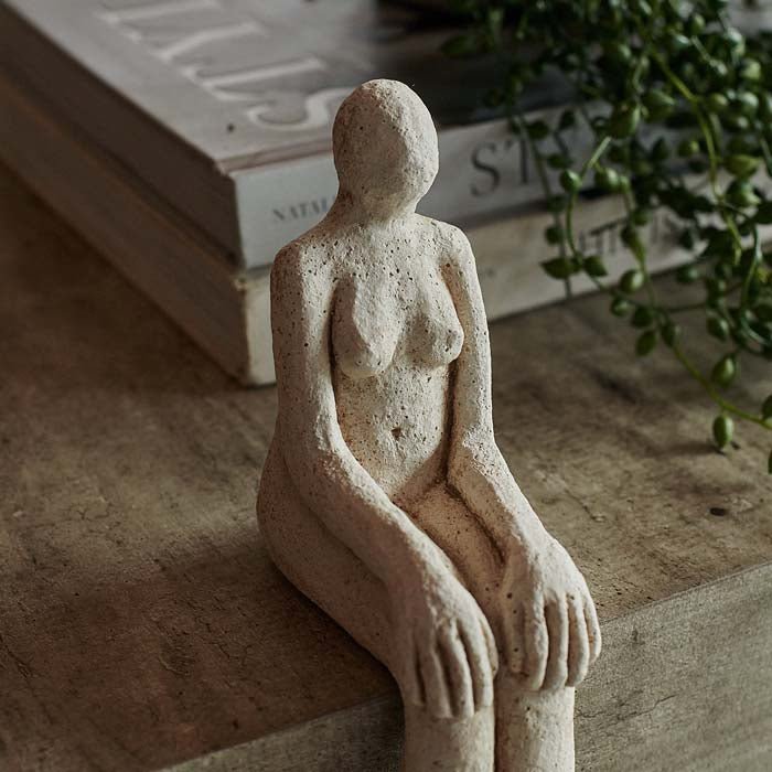 Figurative cement sculpture in seated position, sitting on edge of coffee table.