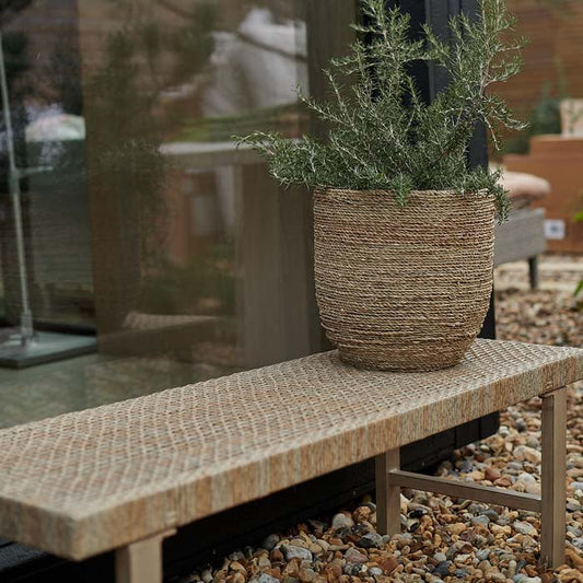 Wicker plant pot displayed on rattan and metal bench in garden.