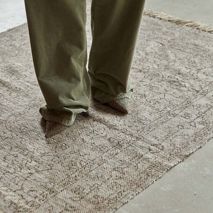 A natural woven jute rug with a subtle floral pattern and someone standing on it.