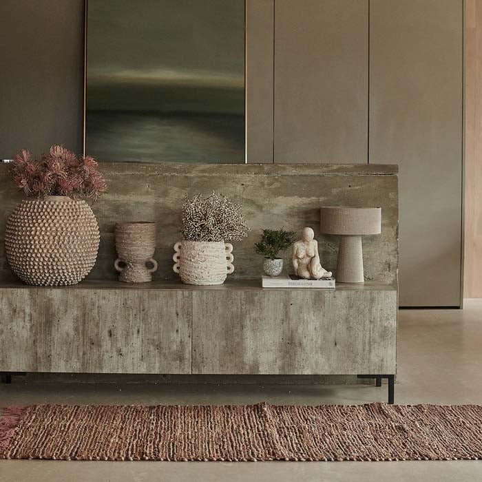 Faux-concrete tv unit, raised on black iron legs, decorated with assortment of stone vases.