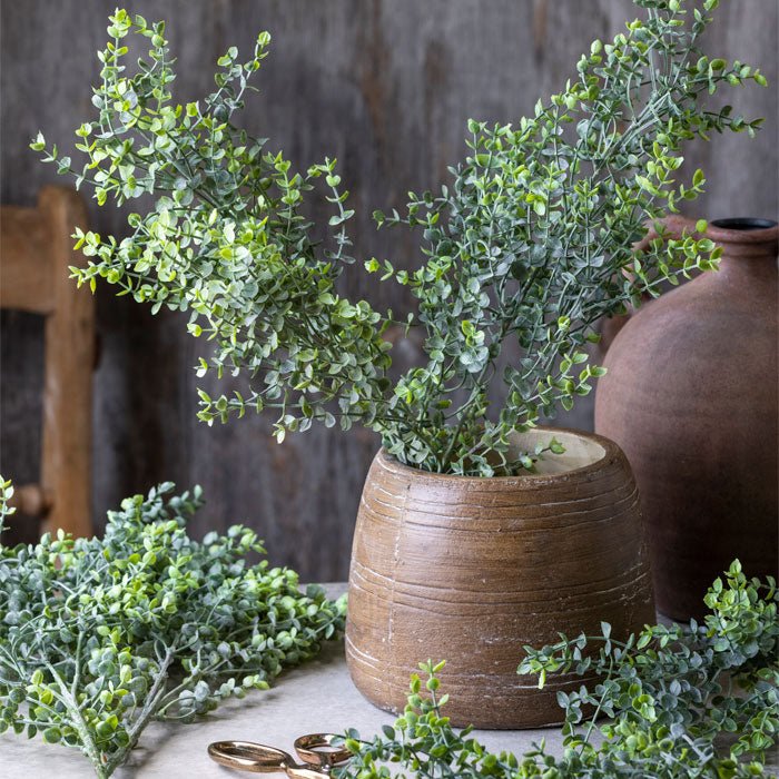 Round brown vase filled with artificial green foliage