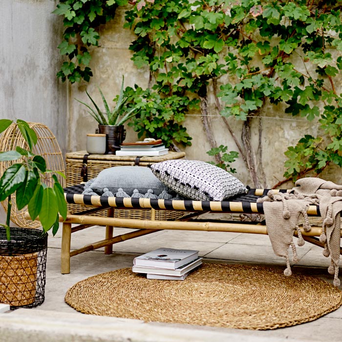 The Levada Daybed in a concrete outdoor patio space, next to a jute rug and styled with cushions.