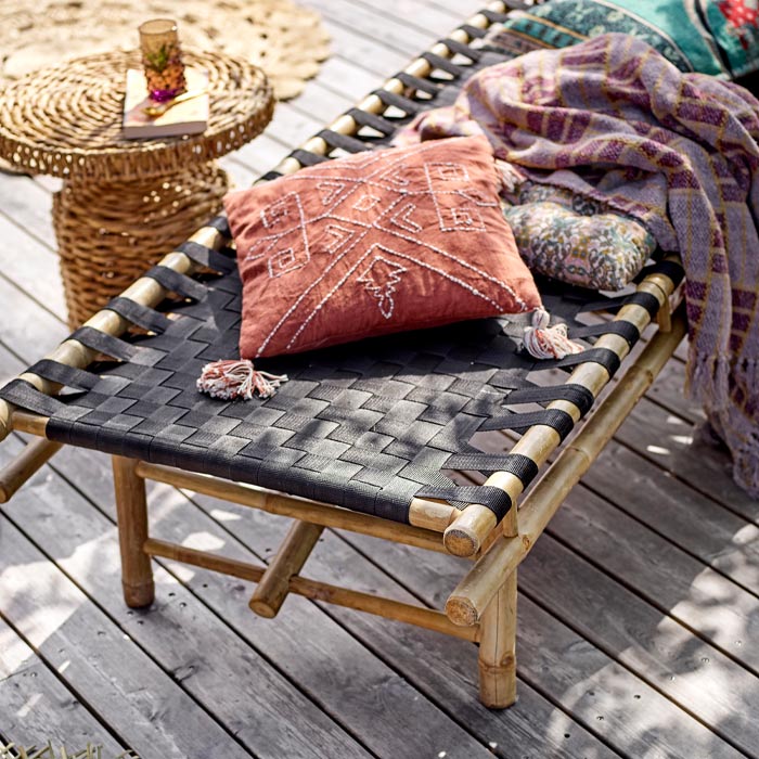 The Levada Daybed on wooden floorboards, accessorised with a red cushion on a sunny day.