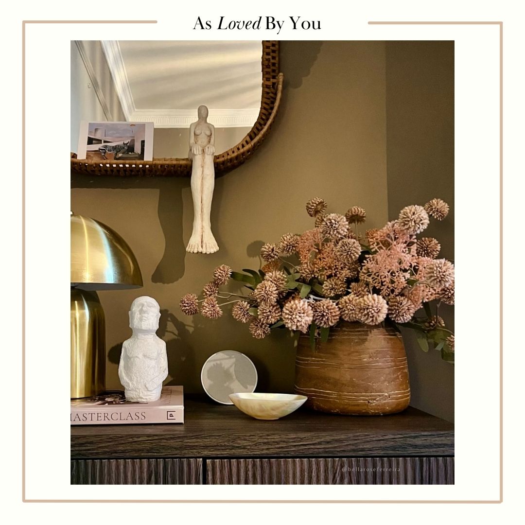 A large brown ceramic vase full of faux flowers on a console next to a couple of ceramic figurative sculptures.