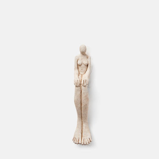 Sitting lady sculpture, with elongated legs, feet and hands, crafted from cement.