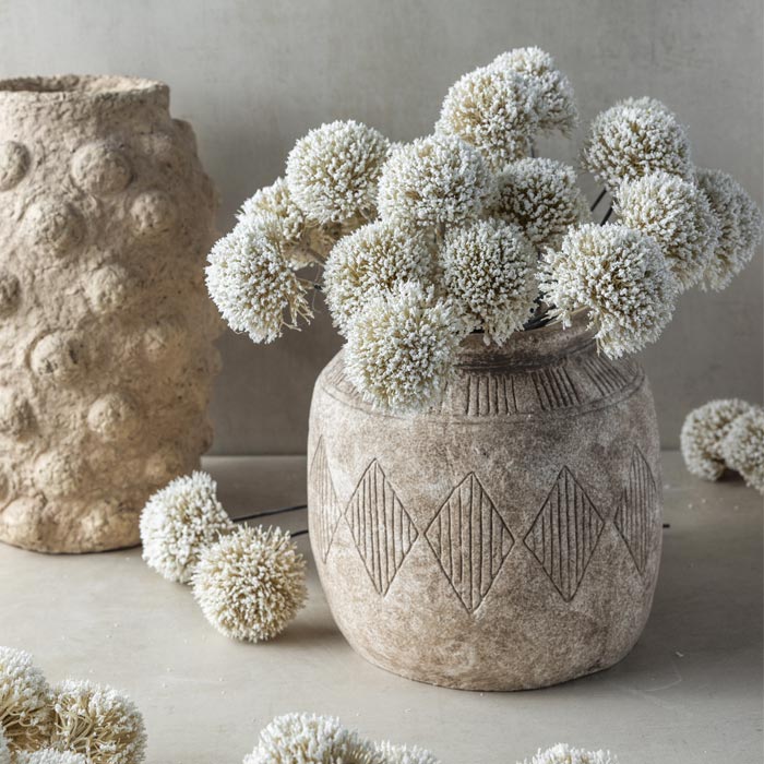 A textured vase filled with luxury artificial allium hand finished flower stem. White round spiky flowers that add lifelike texture to vases. Realistic round ornamental flower stem to add a natural look to flower bouquets. Luxury artificial flowers that look lifelike from Abigail Ahern known for boundary pushing designs. White allium flowers that look like they have been hand picked from the garden.