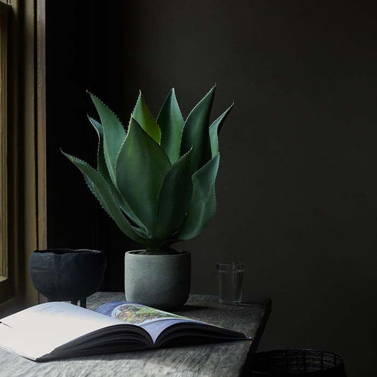 Tall faux aloe vera plant in a grey pot sat on a wooden desk