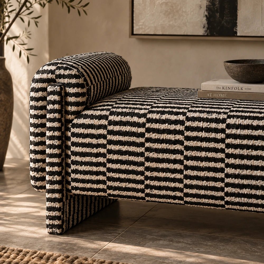 Alvarez Upholstered Bench with pale textured upholstery and wooden frame, styled in a warm neutral living room with layered cushions, side table and soft furnishings.