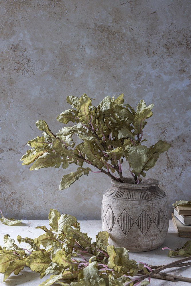 An arrangement of leafy faux foliage arranged in a patterned ceramic vase.