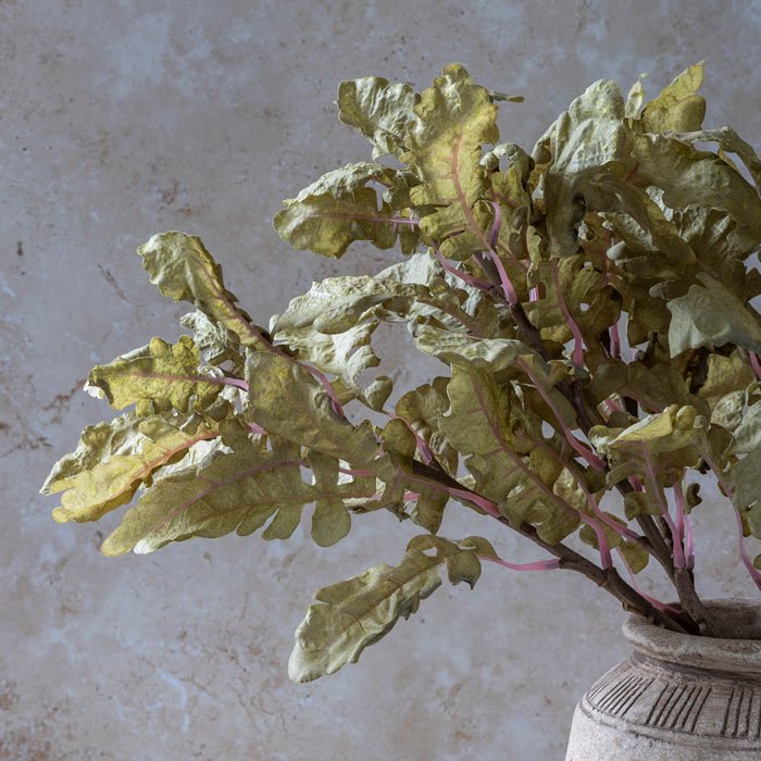Several leafy stems of faux ragwort arranged in a vase.