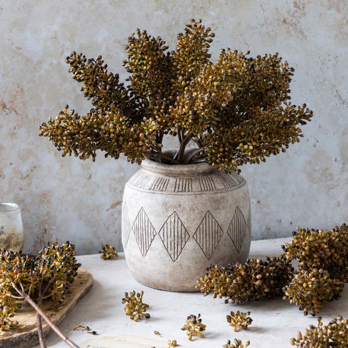 Several stems of faux sorghum umber arranged in a curved cement vase.