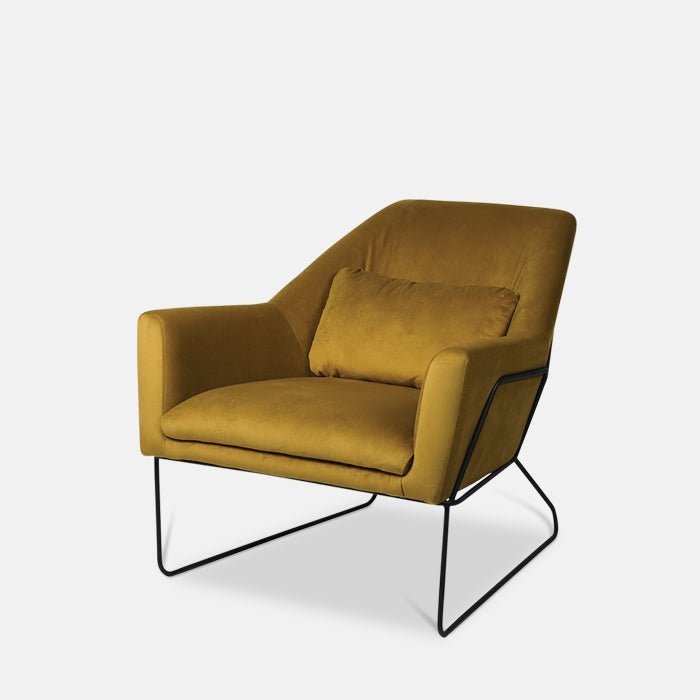 A cutout of the Atura Occasional Chair, a large angular yellow velvet armchair with a black metal frame and metal legs.