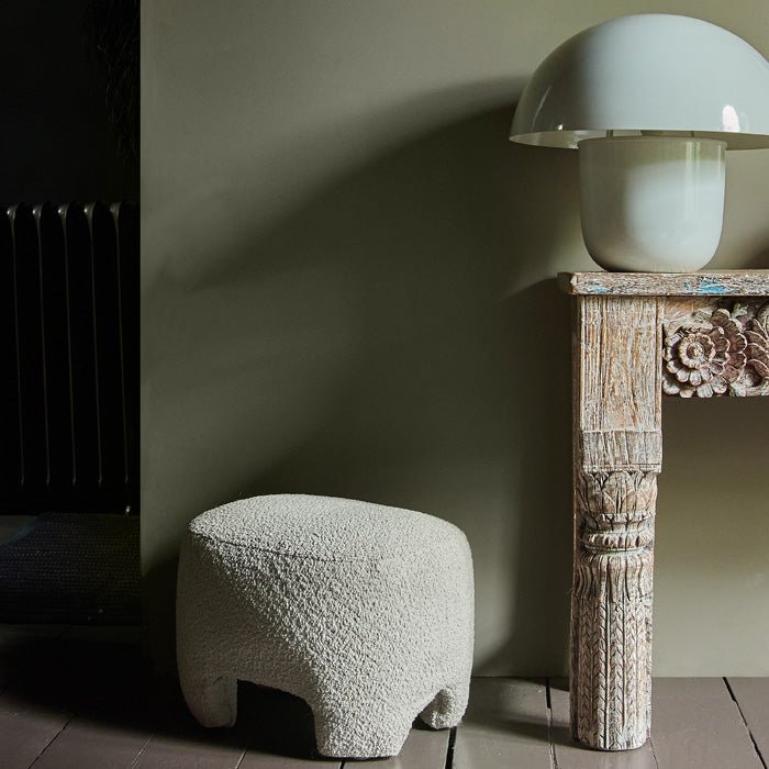 Small white footstool next to a wooden console in front of a brown painted background