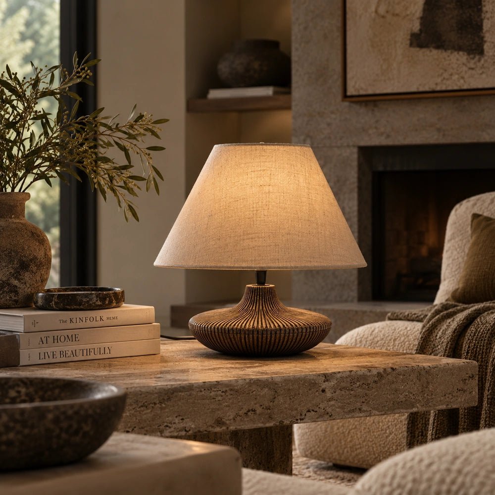 Ballard Wooden Table Lamp with sculptural wood base and neutral shade, glowing beside a bed in a warm layered contemporary bedroom.