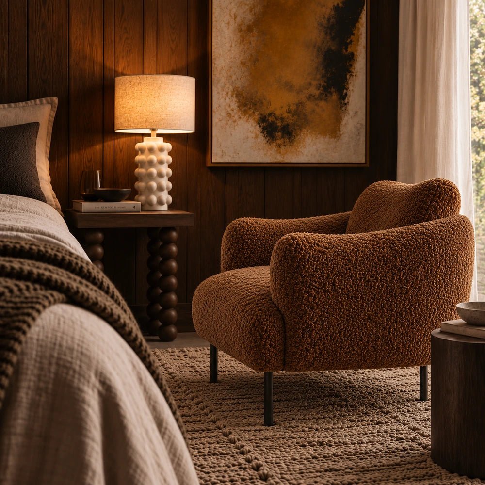 Belville Armchair in toffee brown upholstery with rounded cushioned silhouette, styled in a warm neutral interior with layered contemporary furnishings.
