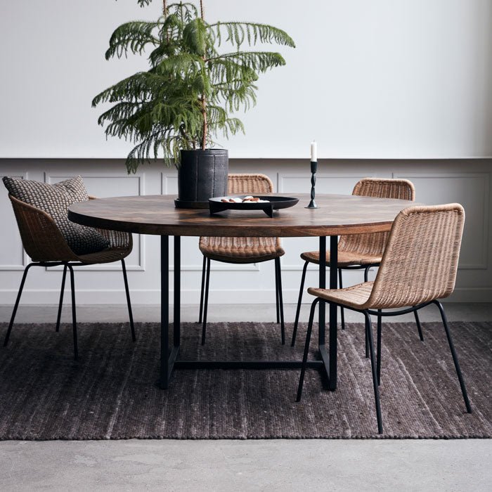 Large round mango wood dining table in warm brown finish, with black metal legs.