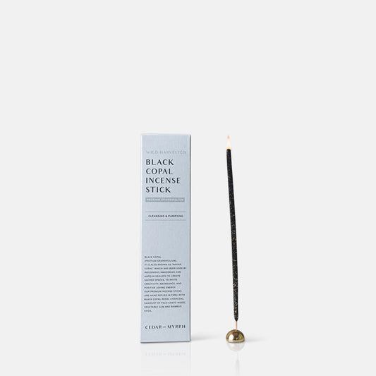 A singe burning incense stick in a small gold holder next to its packaging