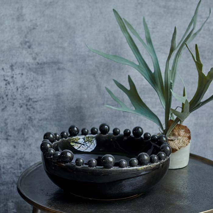 The Bourton Bowl - Black, a large round bowl with a glossy glazed finish and textural bubble top, next to a potted fern.