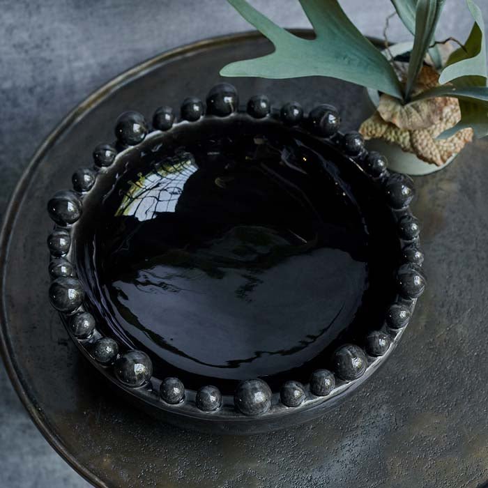 Round bowl with a decorative rim in a glossy black glaze sat on a metal table
