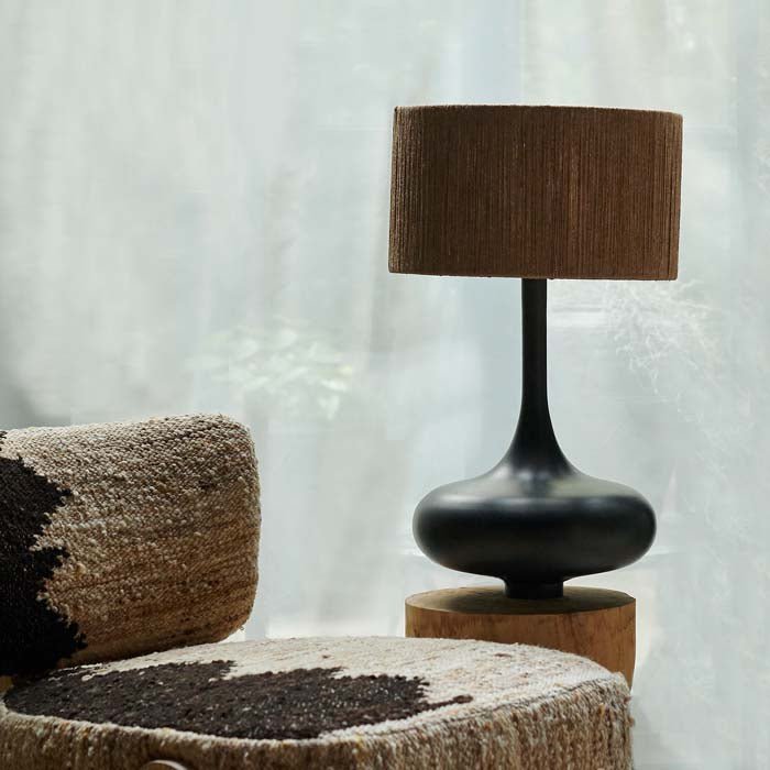 Brooklyn Table Lamp, a sculptural black curvy table lamp with a jute shade styled on a side table next to a textural chair.
