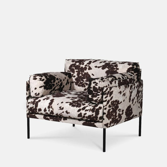 A large textured armchair in a cream and brown cow print pattern with black metal legs.