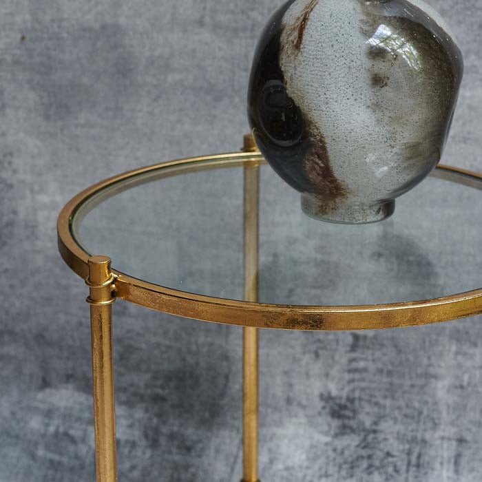 Round clear glass table top with a gold iron frame and a glass vase on top