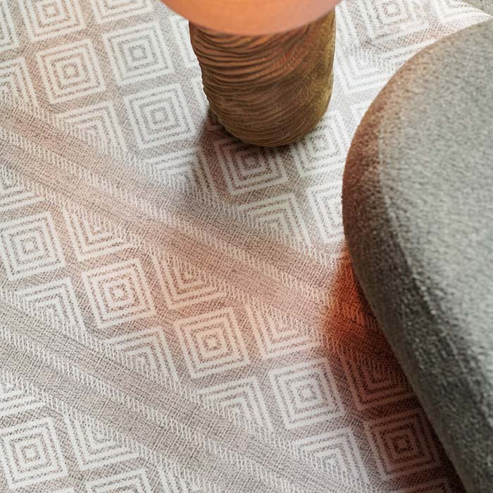 A close up of the Canta Vinyl Flooring, a brown diamond and striped pattern vinyl rug under a floor lamp and a green chair.