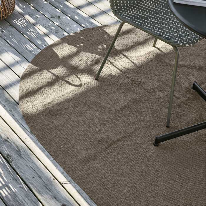 Oval shaped olive green rug placed under an outdoor chair and table