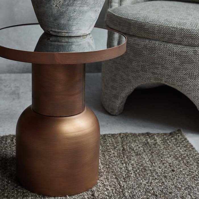 Bronze table with a mirrored top sat on a brown woven rug